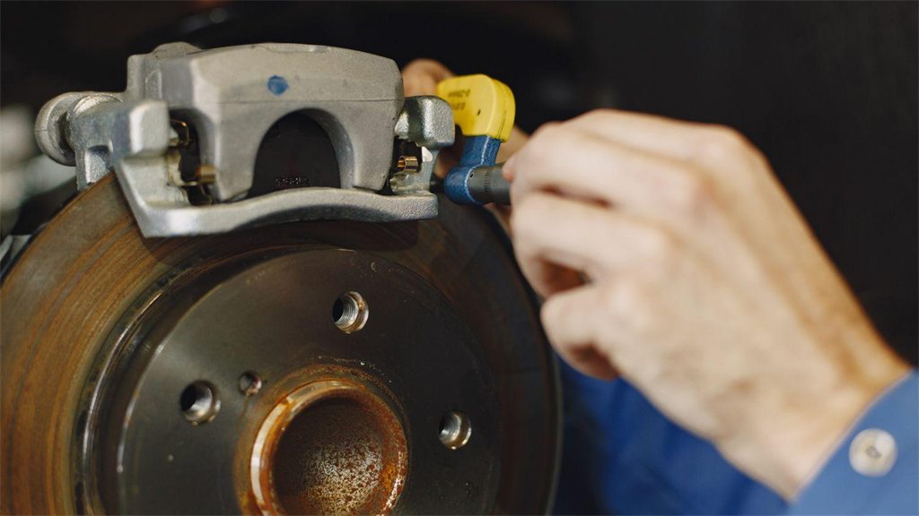 Mão trabalhando no disco de freio e no cubo de roda de um carro