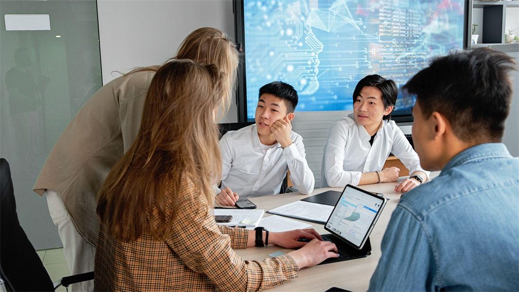 Grupo de jovens reunido em volta de uma mesa olhando um notebook