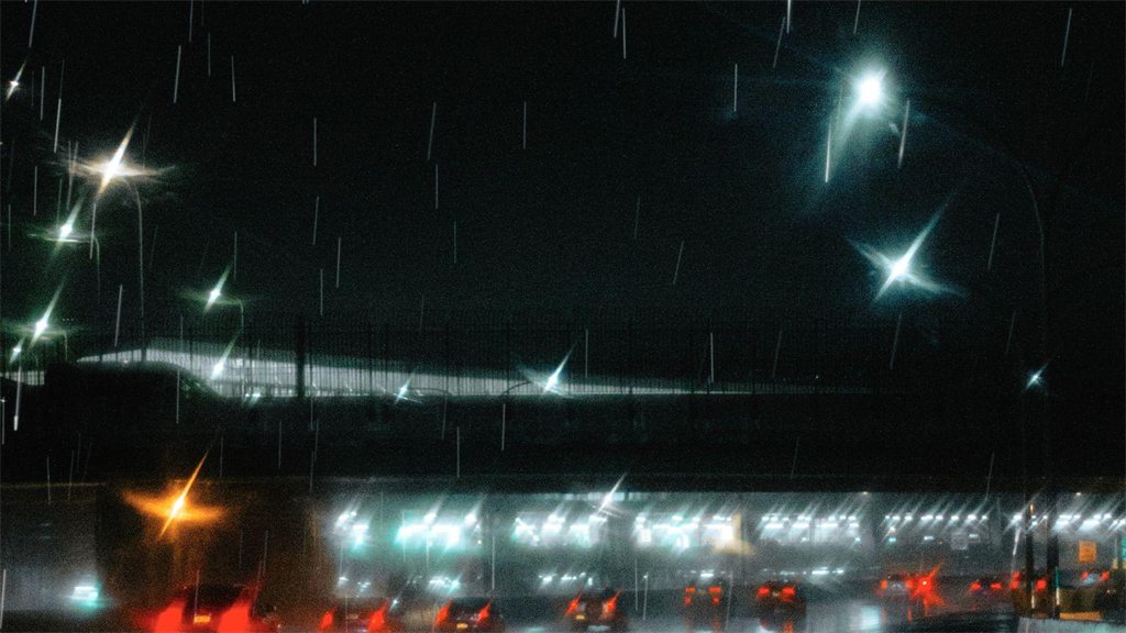Posto de combustível iluminado à noite, visto da rua molhada de chuva