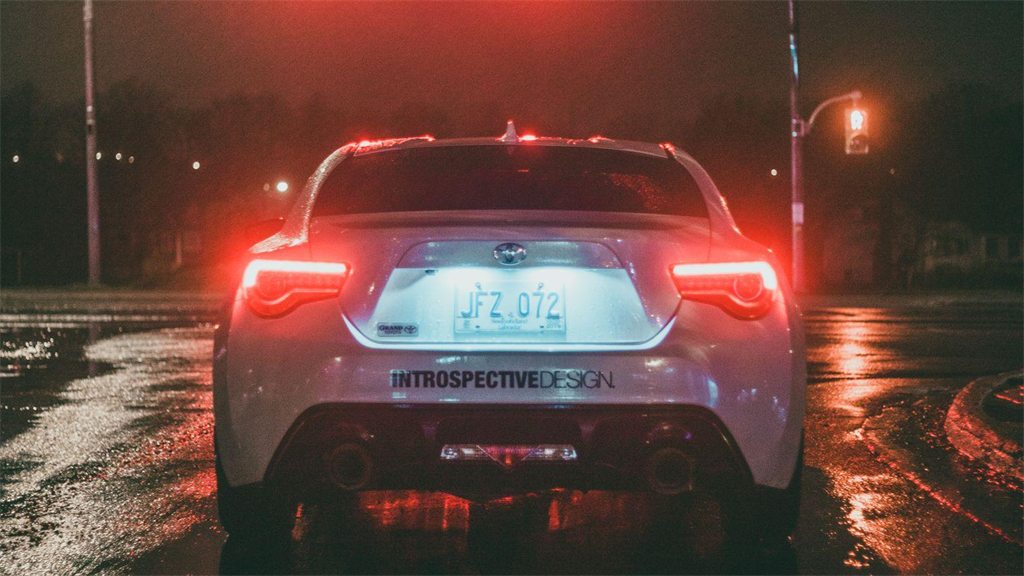 Traseira de um carro com as luzes de freio acesas em via molhada