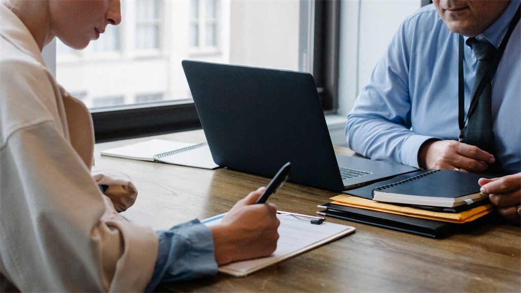 Duas pessoas em reunião de trabalho com notebook e anotações sobre a mesa