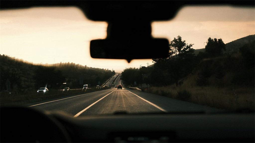 Estrada reta ao entardecer vista de dentro do carro, pelo para-brisa