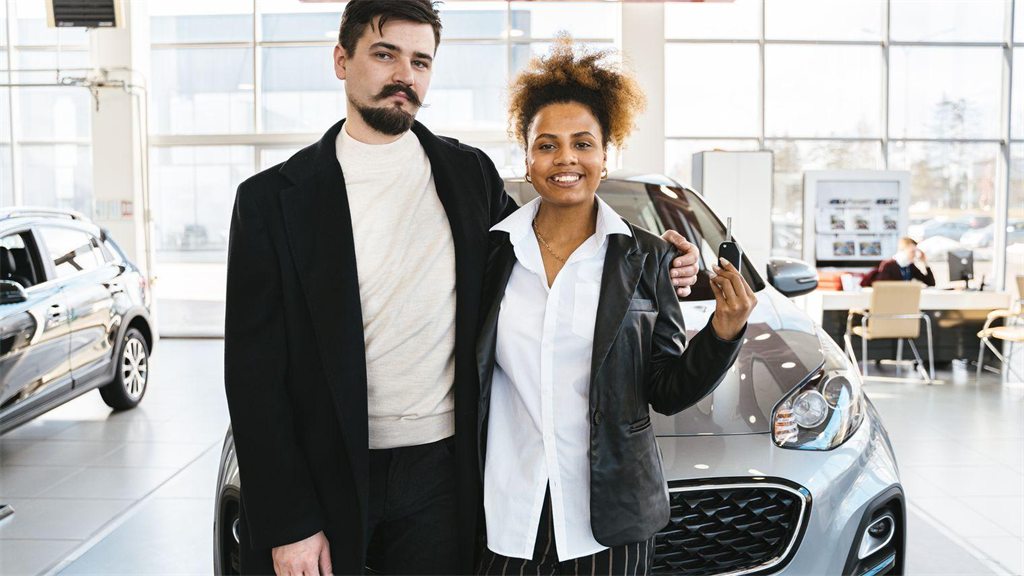 Casal sorrindo ao lado de um carro em uma concessionária