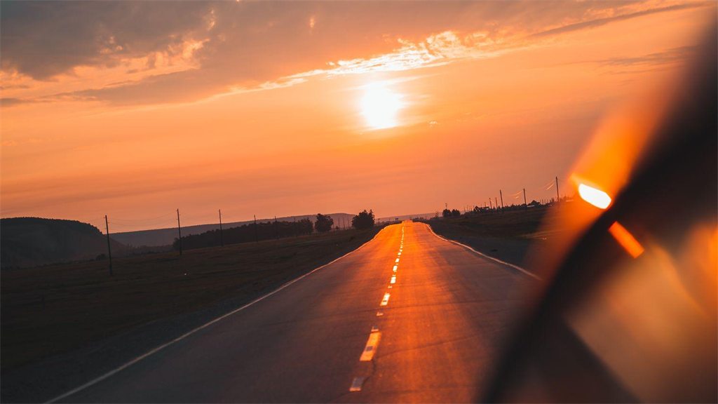 Estrada ao pôr do sol vista de dentro do carro, pelo para-brisa