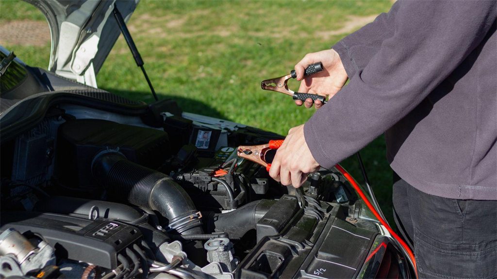 Pessoa mexendo no compartimento do motor de um carro com o capô aberto