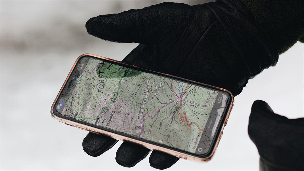Mão com luva preta segurando um celular com um mapa na tela