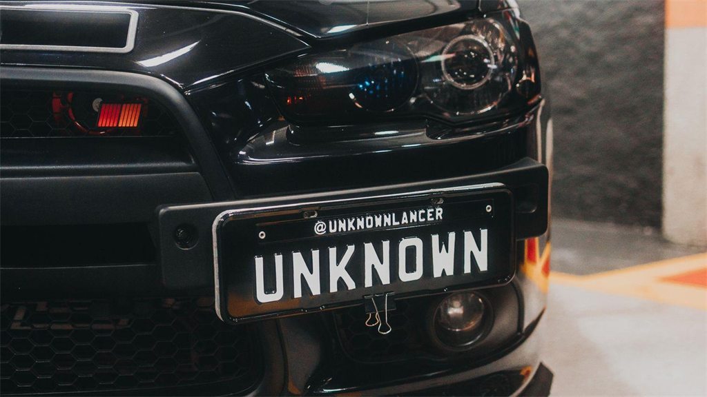 Traseira de um carro escuro com a placa em destaque