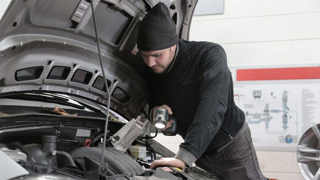Mecânico trabalhando sobre o motor de um carro com o capô aberto