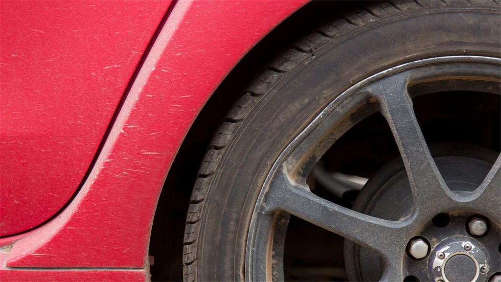 Roda e para-lama de um carro vermelho, vistos de perto