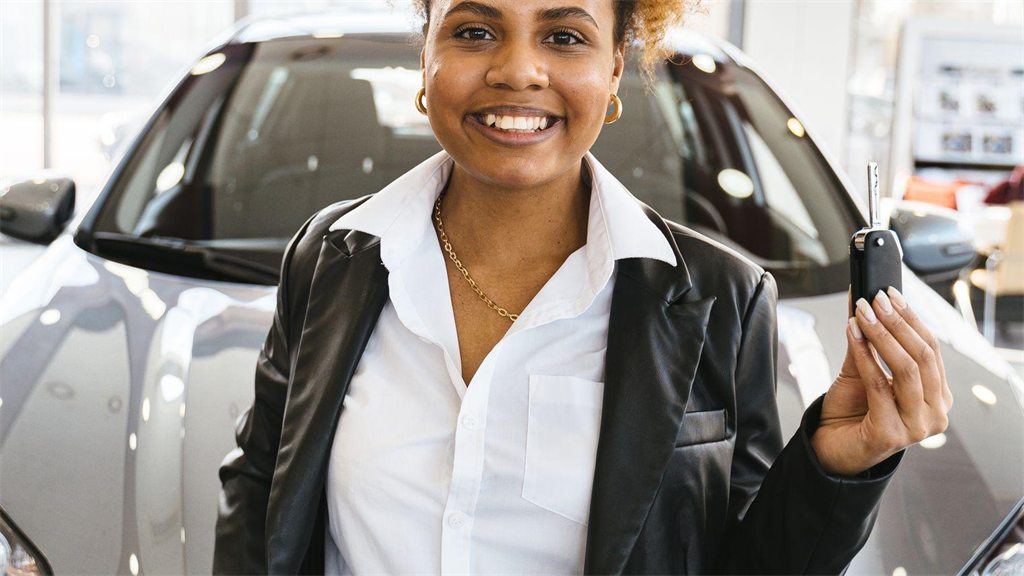 Mulher sorridente segurando a chave ao lado de um carro
